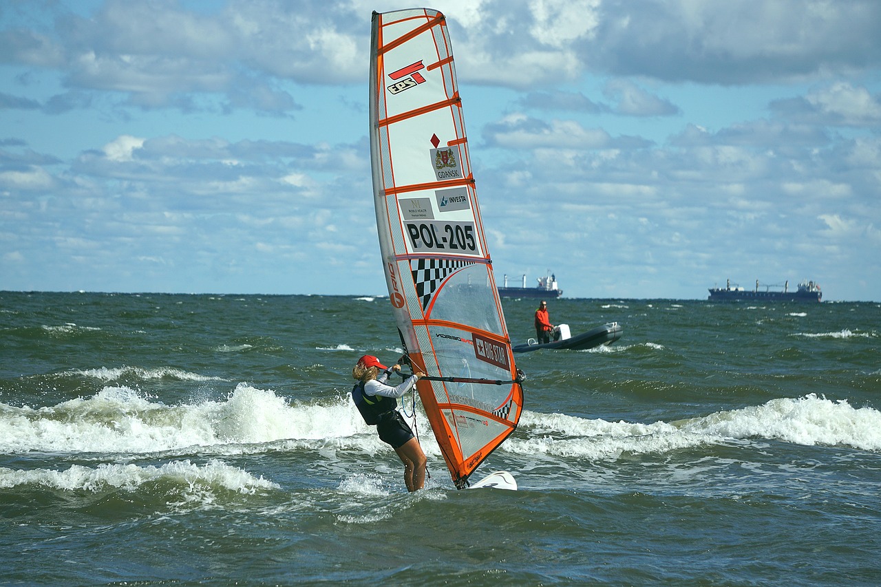 An image showcasing the exhilarating world of windsurfing: a skilled windsurfer, harnessing the vibrant power of the wind, gliding gracefully across the rippling azure waters, under a clear blue sky